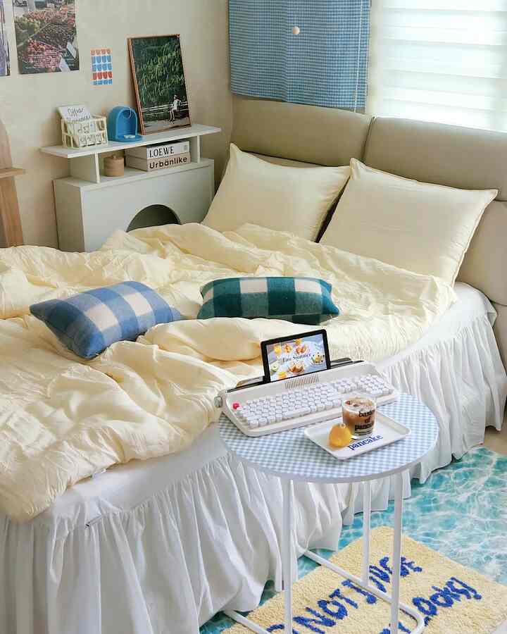 アイボリーとブルーのトーンの寝室、枕とクッションが置かれたベッドとチェック柄の小さなテーブルがある雰囲気の良い空間