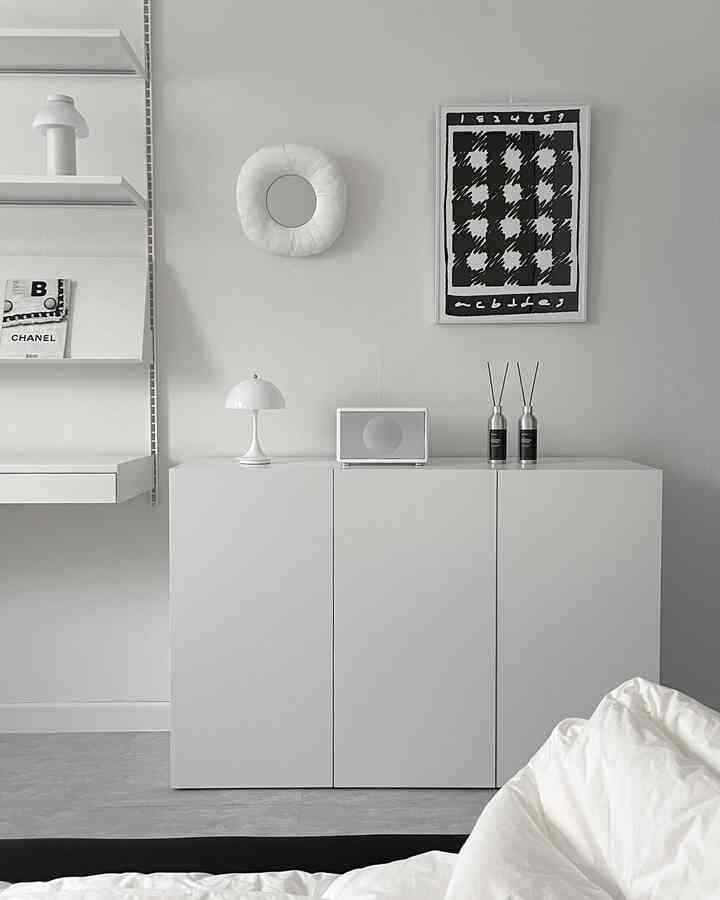 Simple living room in white and gray tones featuring a white dresser topped with table lamp and diffusers, with a monochrome poster on the wall