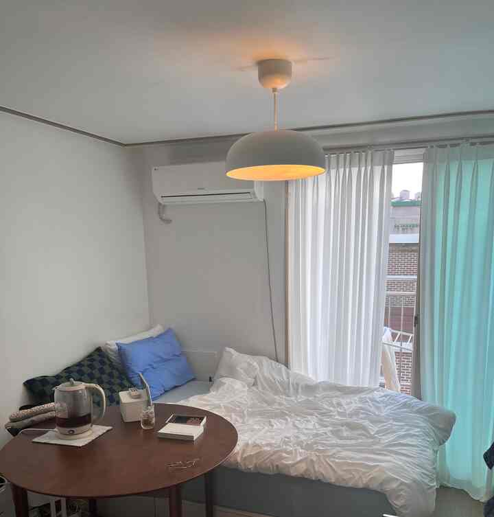 White and brown toned studio bedroom featuring a round table and bed with cozy atmosphere