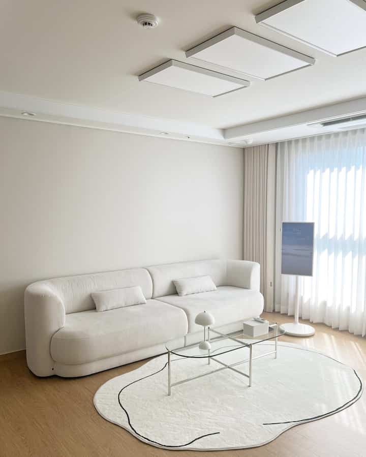 A modern and simple living room in white and natural tones, featuring a curved sofa and a transparent coffee table