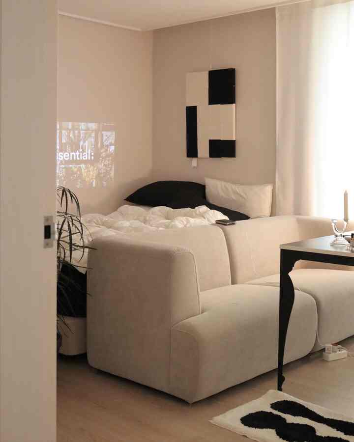 ベージュ色調の寝室、3人掛けソファと白いカーテンが調和したシンプルなインテリア