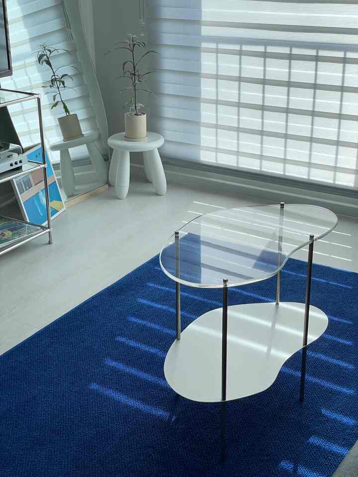 白と青のトーンのリビング、明るい日差しの中に透明なアクリルのティーテーブルと植物が配置されたミッドセンチュリーモダンスタイルのインテリア