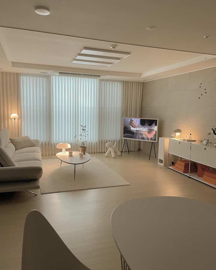 Beige and white toned living room featuring a sofa, coffee table, floor lamp by window, and a plant, creating a cozy modern interior