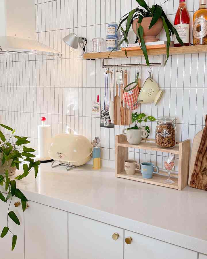 White tiled kitchen with wood tone shelves and plants, featuring a clean and cozy atmosphere