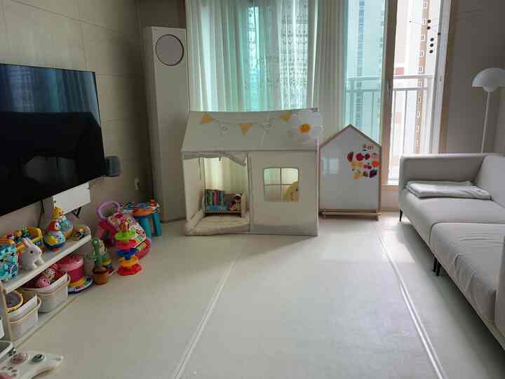 Beige and white toned living room kids' space featuring sofa, play tent, and children's toys in a bright, organized setting