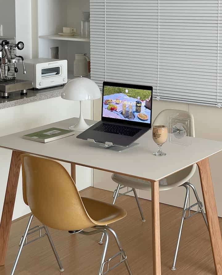 Modern kitchen and home cafe space featuring white and wood tones with a desk holding a laptop and coffee glass