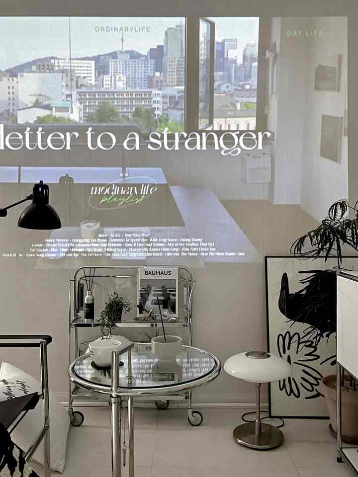 Modern living room with white and chrome tones, featuring a round glass side table, floor lamp, large potted plant, and framed artwork in a neat setting