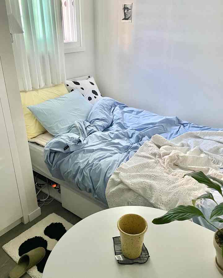 白い壁と青い寝具が配置されたワンルームの寝室、シンプルで居心地の良い空間