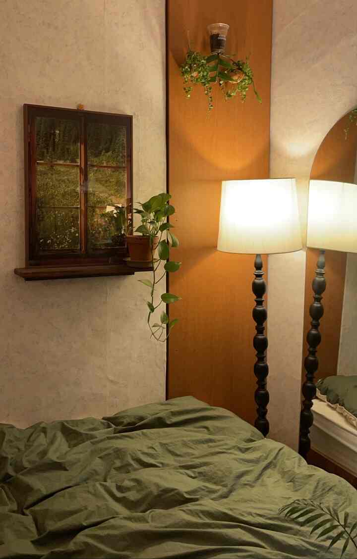 ブラウンの木パネルとグリーンの寝具、フロアランプとポスターが配置された雰囲気のある寝室