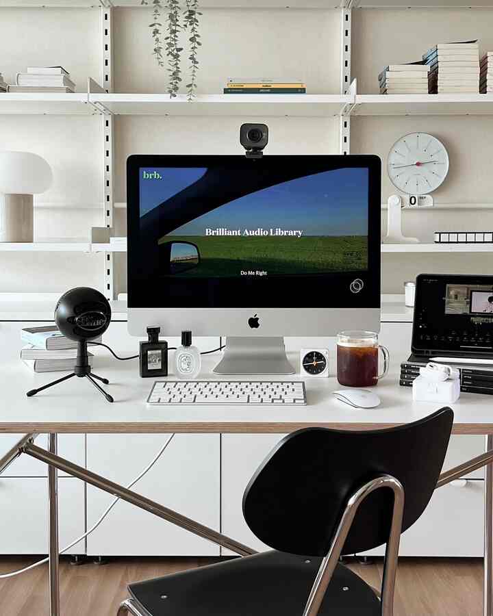 Modern home office in white tone featuring a desk with iMac, black microphone, and webcam in a neat workspace