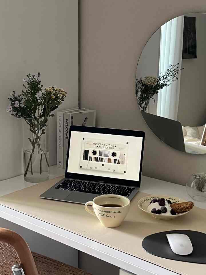 白を基調としたワンルームのデスク空間、ノートパソコンとコーヒーカップ、花が置かれたシンプルで清潔感のあるインテリア