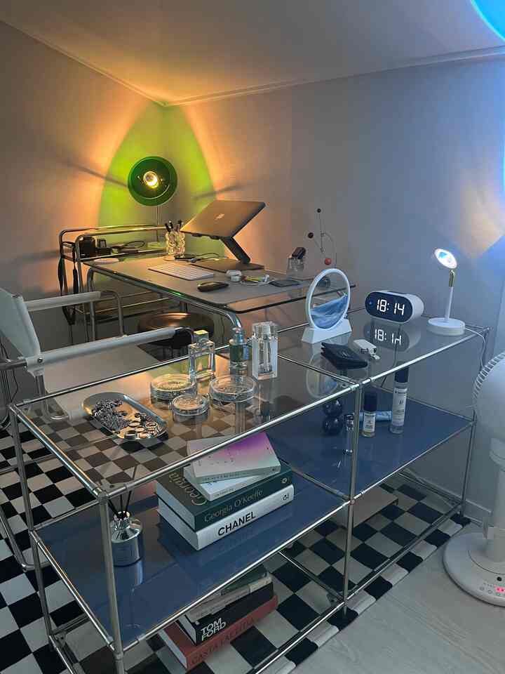 白い壁と黒白のチェッカー柄ラグがあるモダンなブルートーンのホームオフィス、透明なガラスのデスクと白い椅子が配置された印象的な空間