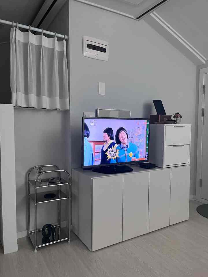 白を基調としたリビング、テレビとモダンなテレビ台、ステンレスのサイドテーブルが配置された印象的な空間