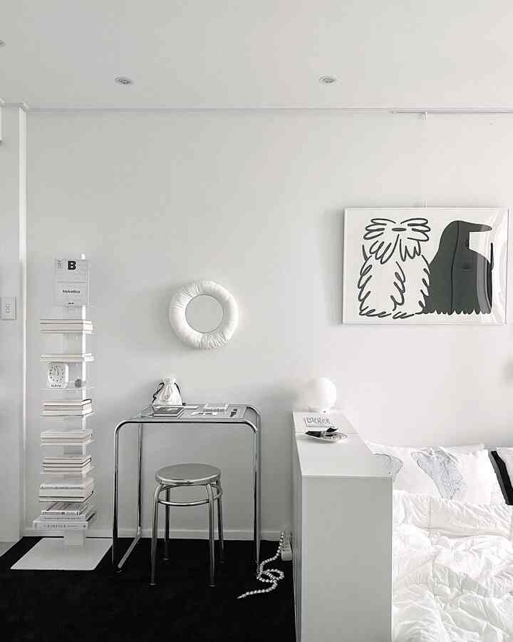 Simple modern home office space in white and black tones featuring stainless round stool, desk, poster, and circular mirror with clean atmosphere