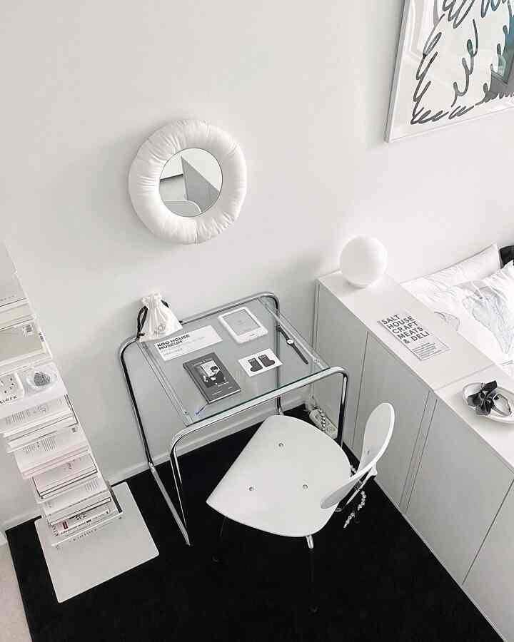 A compact white and black toned home office featuring a minimal glass desk and uniquely designed chair in a clean interior setting