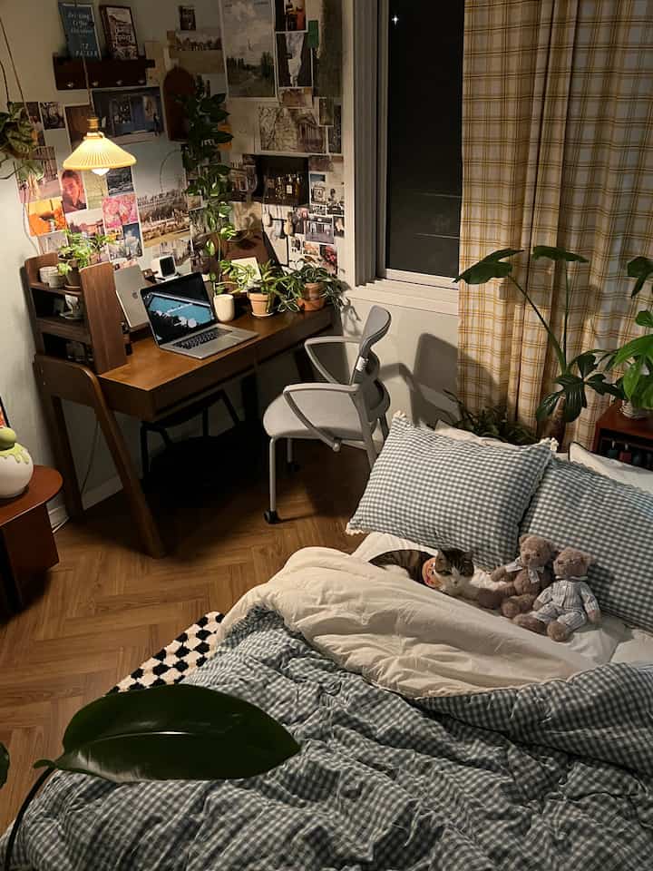 Cozy kids' room study with yellow checkered curtain, wooden desk, plants, and a cat resting on the bed