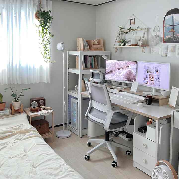 White and natural wood-toned bedroom combined with home office, featuring desk, chair, window curtains, and plants creating a clean atmosphere
