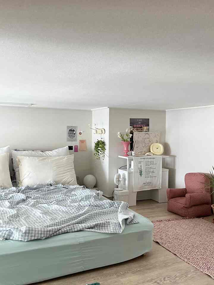 ナチュラルカラーとブルーが調和したワンルームの寝室、大きなベッドと赤いレトロなアームチェアが配置された印象的な空間