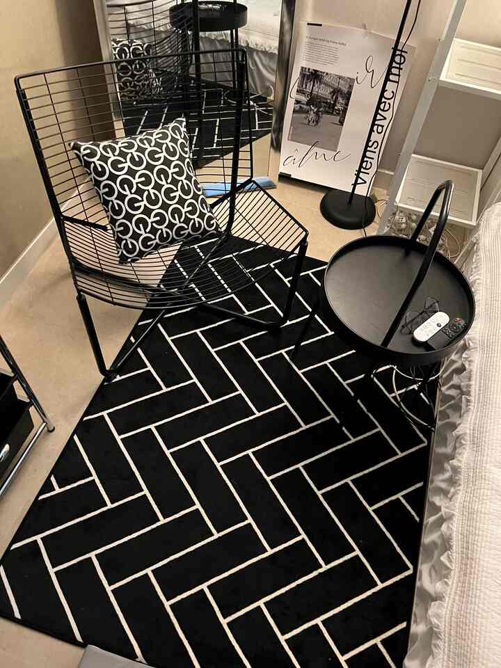 ブラックとナチュラルトーンの寝室、メタルワイヤーチェアとナイトテーブル、パターンクッションが調和したモダンな空間