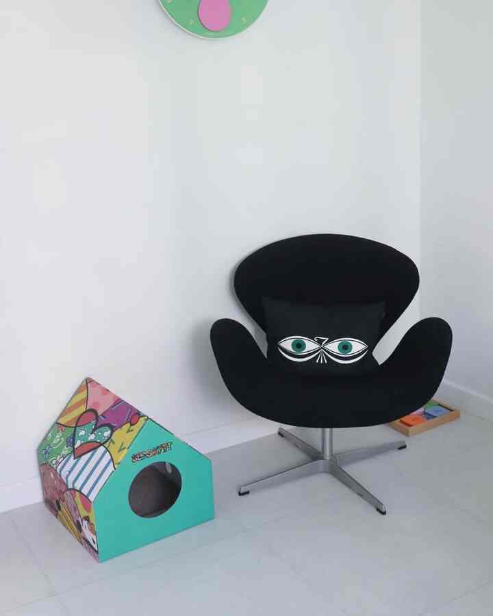 Minimal living room with white walls, black armchair, and colorful cat house
