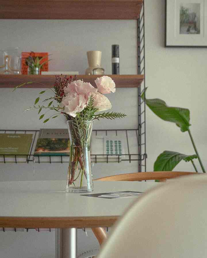 Beige and white toned kitchen-adjacent dining space featuring a round table with a vase of flowers and plants, creating cozy atmosphere