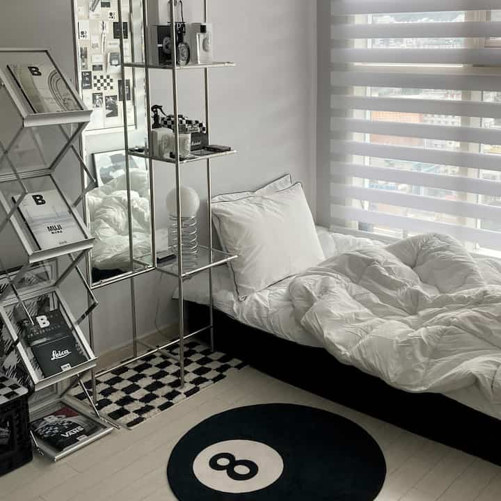Monotone bedroom in white and black, featuring a bookshelf on the side and a circular 8-ball rug, creating a clean interior atmosphere