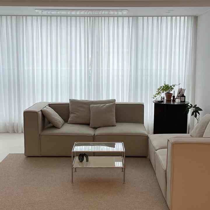 Beige-toned living room featuring beige modular sofa, brown rug, and white curtains in a natural modern style