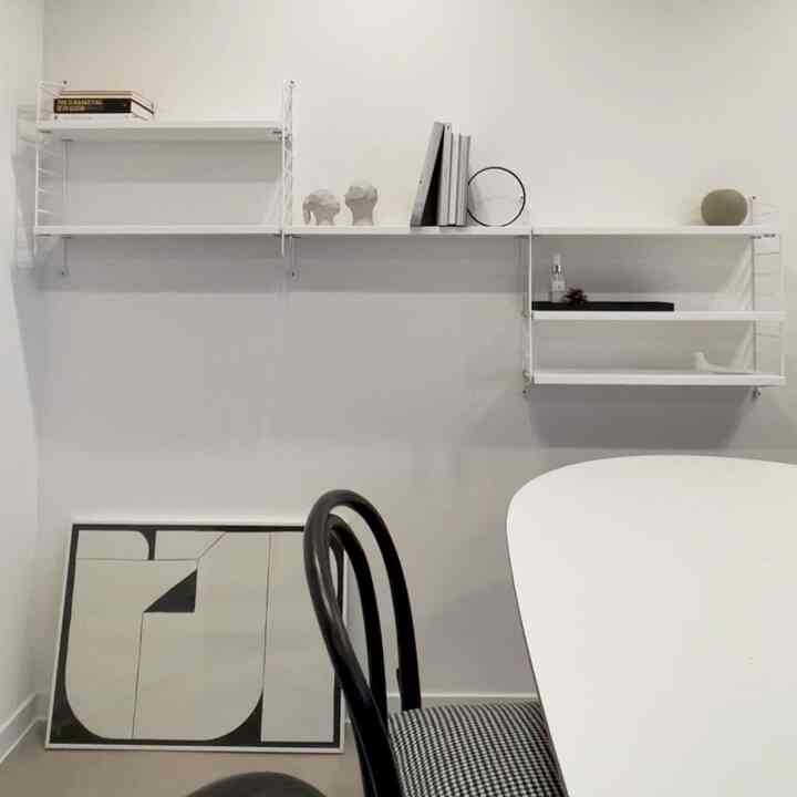 Minimal Nordic style space in white and black tones featuring wall-mounted string shelves and a modern dining chair with a clean aesthetic