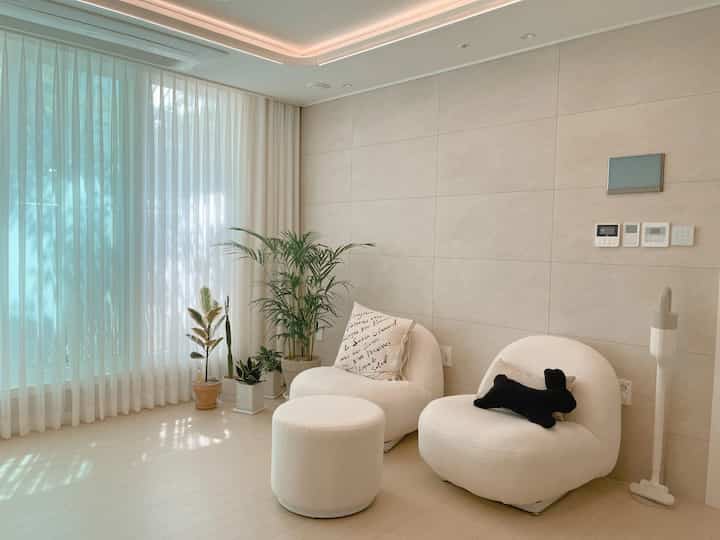 White-toned small living room featuring cozy rounded armchairs and lush plants creating a warm atmosphere