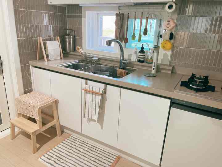 Clean kitchen with white cabinets and wood tones, featuring a stool and a door mat creating a cozy atmosphere
