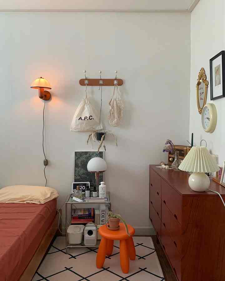 Beige and orange toned bedroom featuring wood dresser, nightstand, wall and table lamps with a warm natural atmosphere