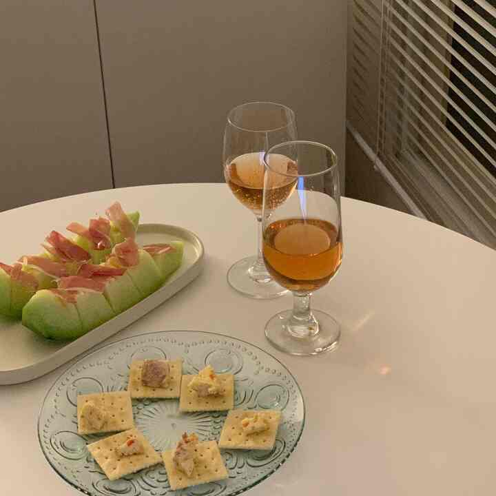 Soft white-toned living or dining area featuring a table with fruit cheese, ham, and rosé wine creating a cozy atmosphere