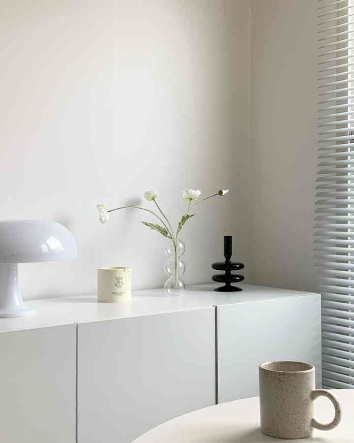 ホワイトトーンのリビング、シンプルなキャビネットの上に花瓶とテーブルランプが置かれた印象的なモダンインテリア