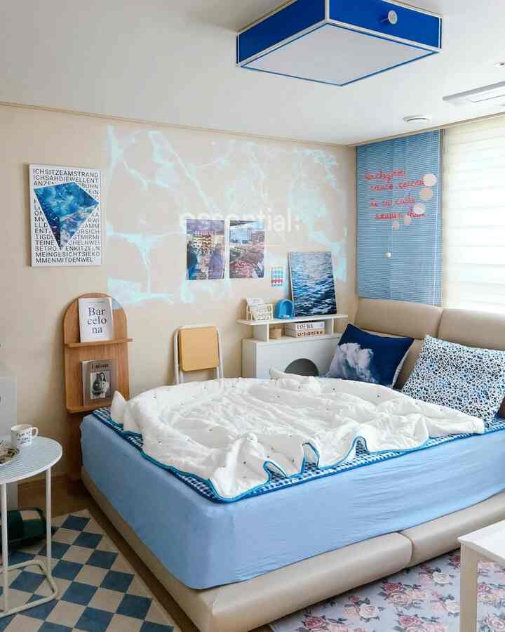 Blue-toned bedroom space featuring a blue bed with white bedding, posters on the wall, and a cozy mid-century modern interior