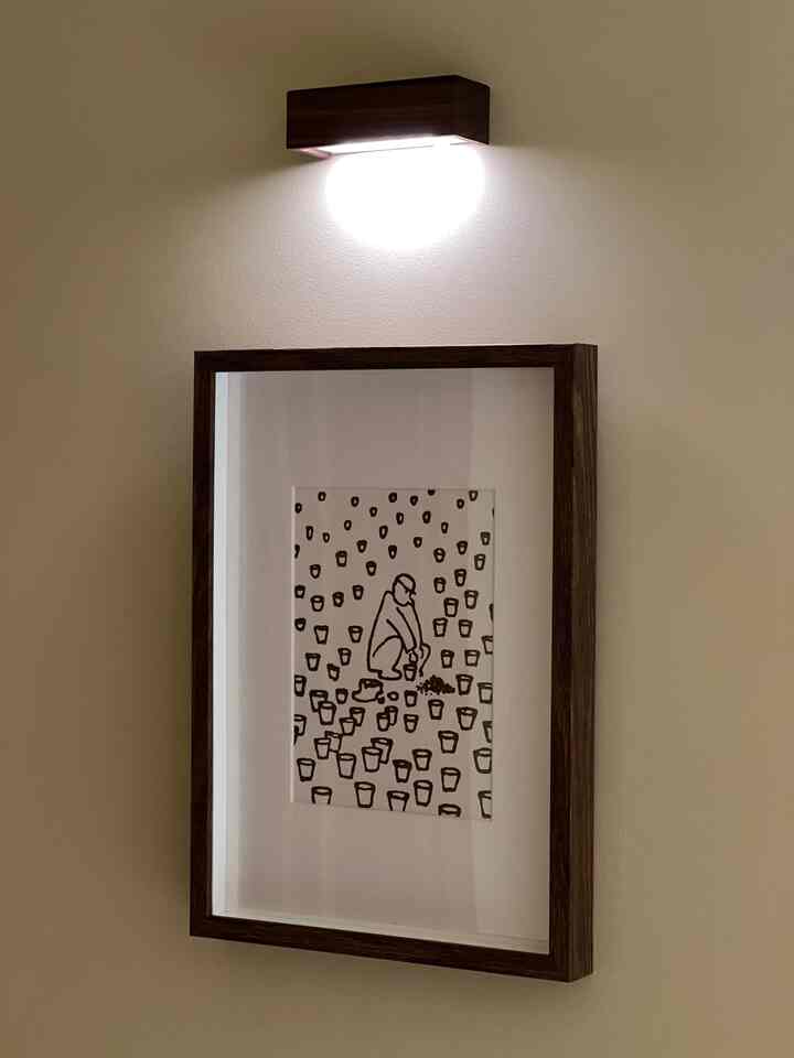 暖かいベージュの壁にブラウンの木製額縁の絵が掛けられ、その上に無線モーションセンサーの壁灯が取り付けられた玄関の空間