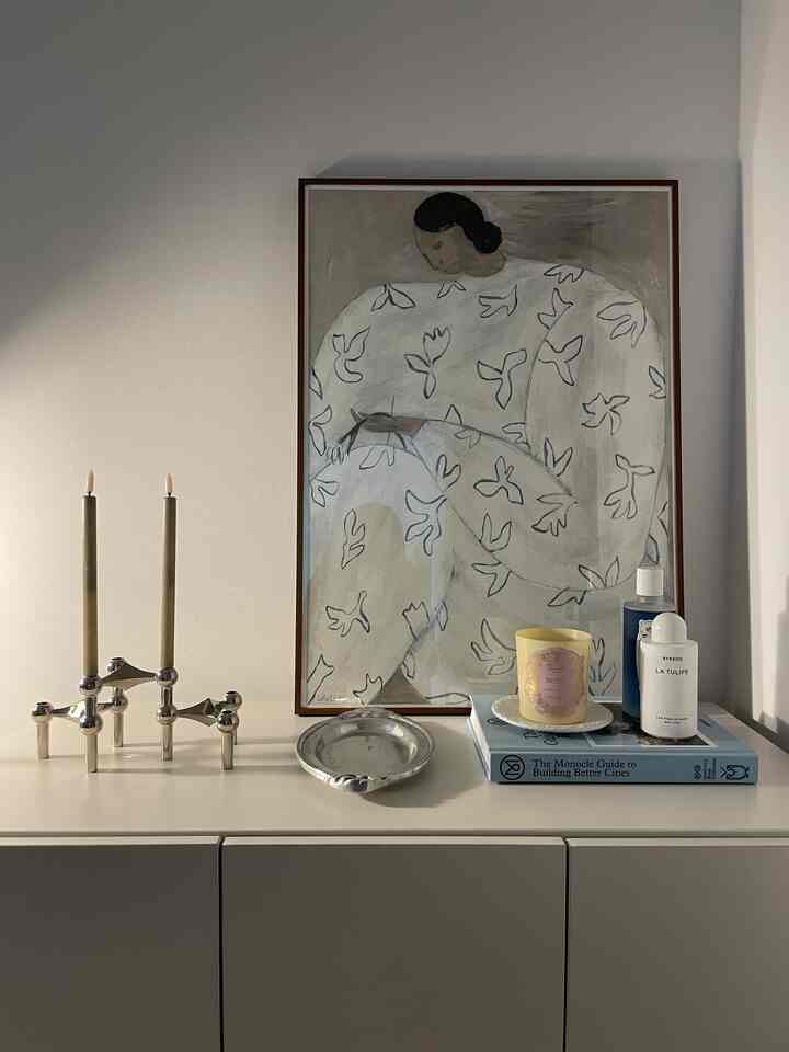 Natural-toned bedroom dresser area featuring white and brown hues with candles, picture frame, and silver tray on top