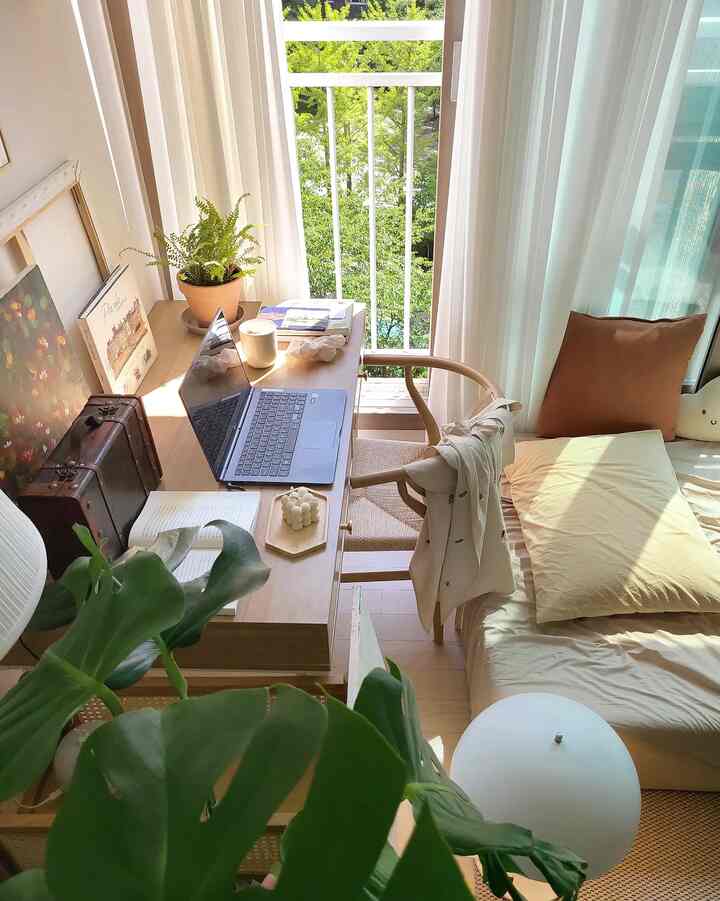 Bright and minimal single-bedroom home office featuring wood tones with a desk and bed next to large window