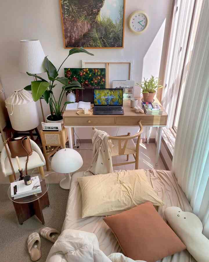 Beige and wood tone studio bedroom featuring desk, chair, pillows, and curtains with a cozy natural atmosphere