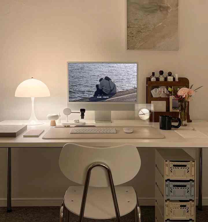 White-toned home office space featuring a central desk with computer and a table lamp on the left, creating a clean study interior