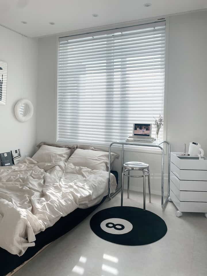 Modern bedroom in white, black, and beige tones featuring bedding and an 8-ball rug with a clean aesthetic