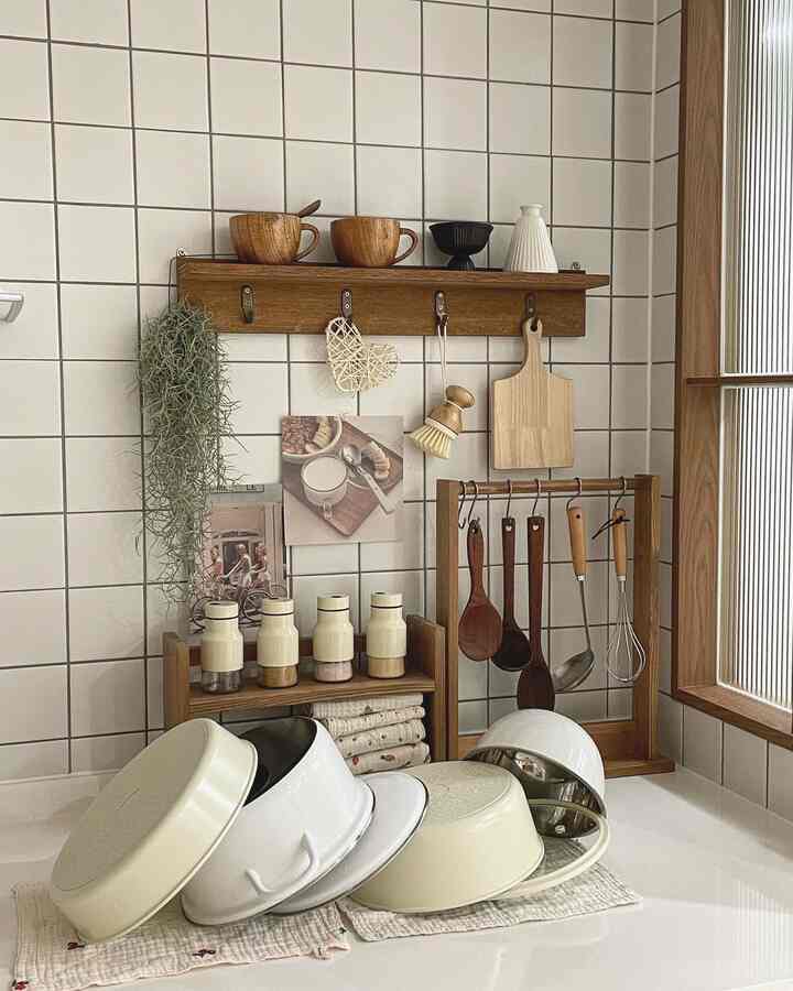 Natural toned kitchen space featuring wooden shelves and utensil racks against white tiled wall with neatly organized pots and kitchen tools