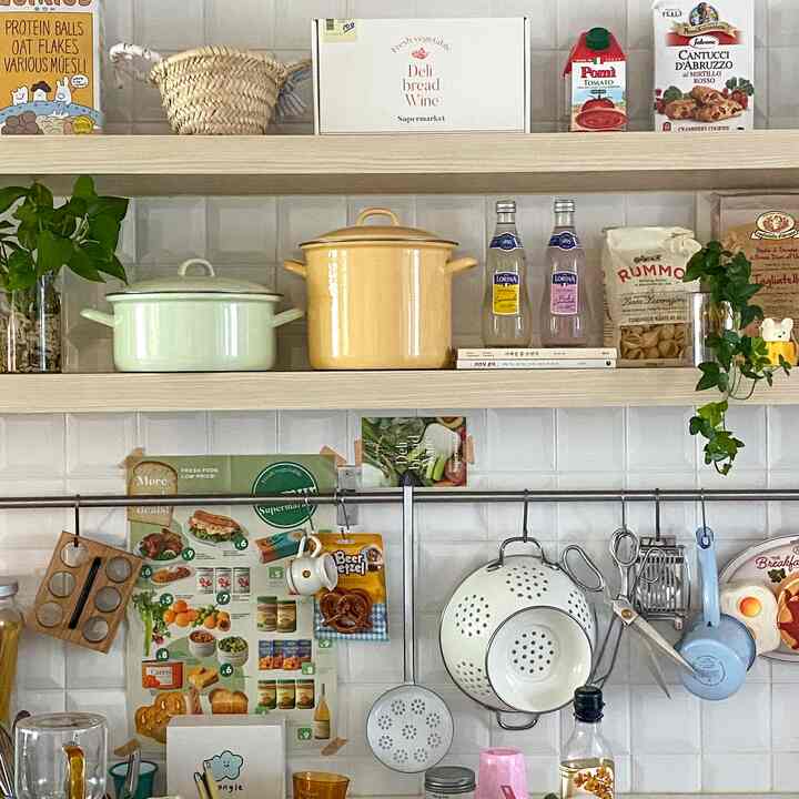 ナチュラルカラーのキッチン空間、木製の棚と様々な食器、ポスターが配置された雰囲気のあるインテリア