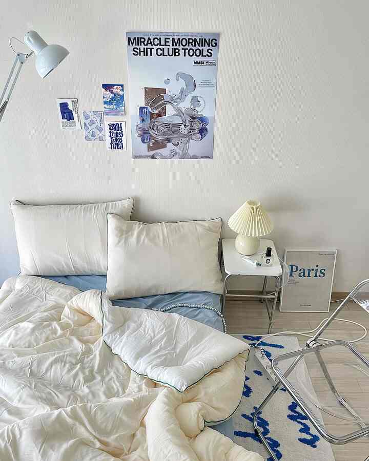White and blue toned studio bedroom featuring cozy bedding and a side table in a clean, modern space