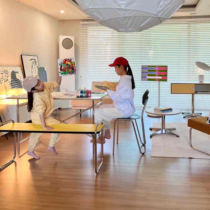 明るい木目調の床と白いブラインドがある子供部屋、ダイニングテーブルで絵を描く二人の子供がいる自然な雰囲気のインテリア