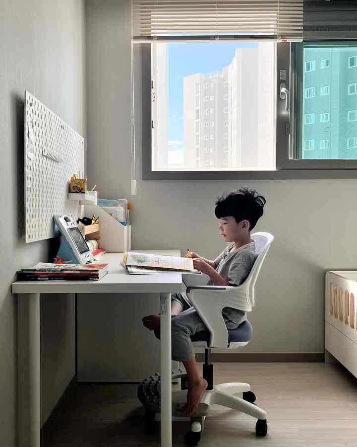 Natural-toned kids' room featuring a white children's desk and chair next to a window in a clean study space