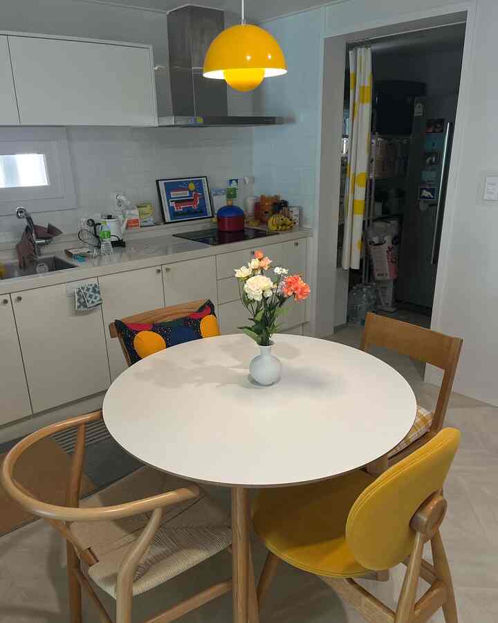 白と黄色のトーンのキッチンとダイニング、木製チェアと丸テーブルに花瓶が置かれた印象的な空間