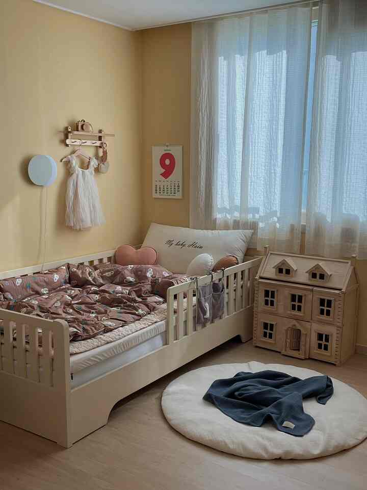 ベージュ色調の子供部屋、ベビーベッドと木製のおもちゃの家が配置された自然で温かみのあるインテリア