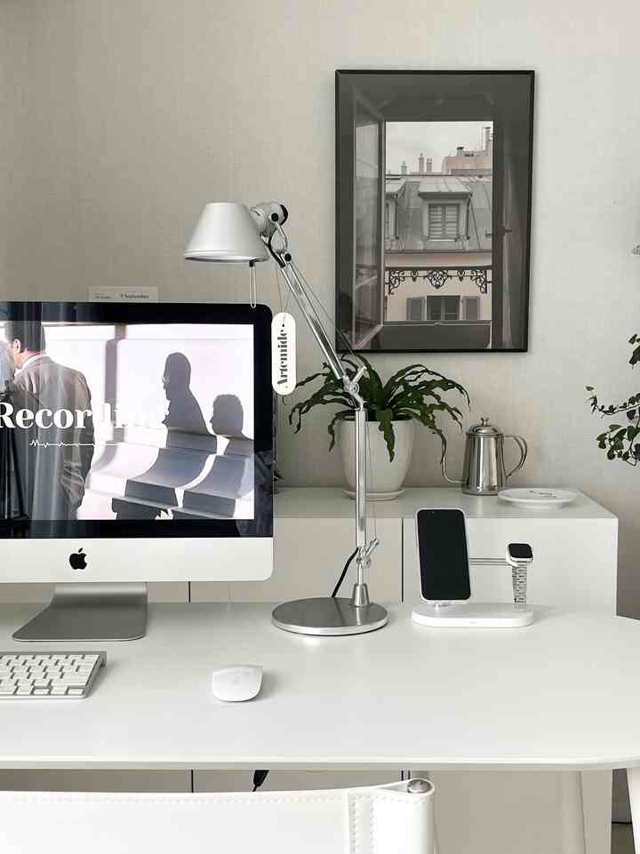 Silver and white toned home office space featuring a desk with iMac monitor, adjustable table lamp, plants and framed art creating a clean workspace
