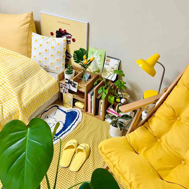 黄色のトーンのコンパクトなリビングルーム、黄色のアームチェアとチェック柄のベッドカバー、植物とフロアランプが配置された雰囲気のあるインテリア