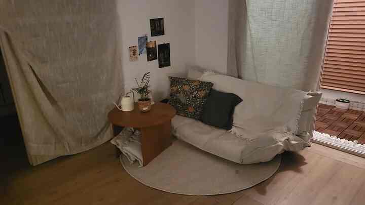 ナチュラルな色調のワンルームリビング、リクライナーソファベッドと丸い木製テーブル、ラウンドラグが落ち着いた印象のインテリア。